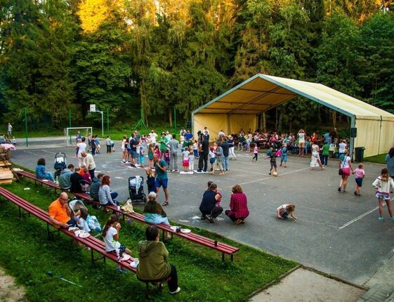 Covered outdoor marquee and picnic benches on a sports court, families dining and children playing amid forested hotel grounds