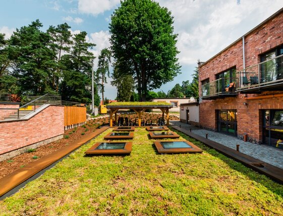 Brick hotel with glass balconies, sedum green roof with skylights, covered outdoor dining area and forested grounds.