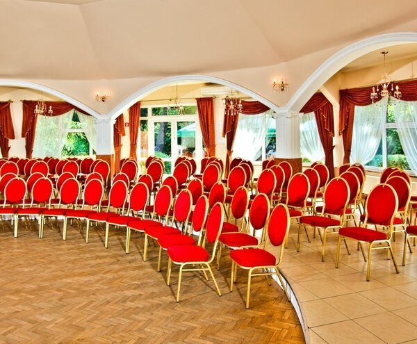 Elegancka sala hotelowa na wydarzenia z rzędami czerwonych krzeseł, łukowymi kolumnami, żyrandolami i widokiem na ogród