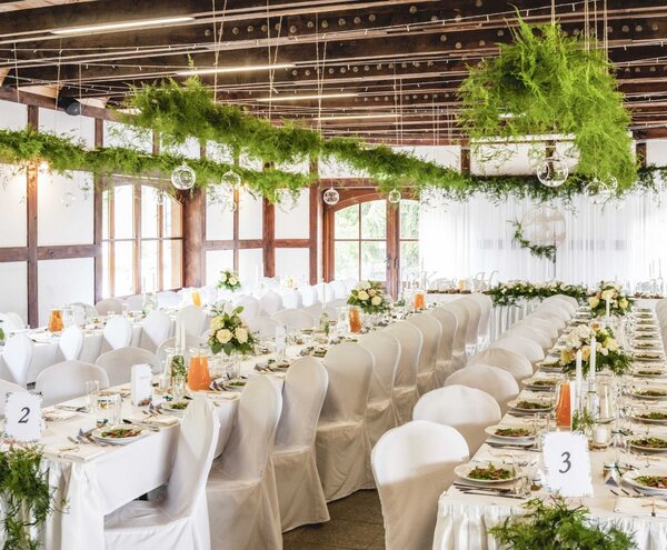 Elegant rustic reception with long white tables, chair covers, floral centerpieces and suspended greenery under wooden beams