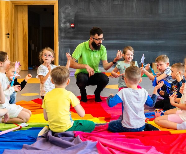 Zajęcia klubu dziecięcego z animatorem prowadzącym prace plastyczne na kolorowej macie w sali zabaw