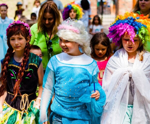 Group of children in colorful costumes and wigs walking outdoors during a lively family-friendly costume parade