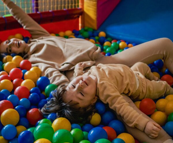 Smiling child and adult sprawled in a colorful indoor ball pit, family-friendly play area with soft padded walls