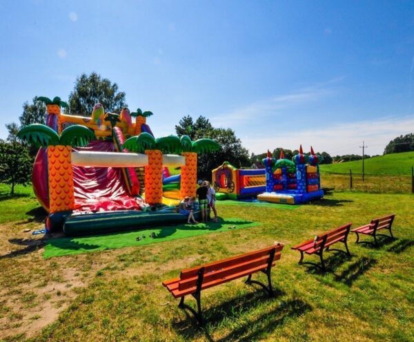 Colorful inflatable slides and bouncy castles with children playing, benches on a sunny lawn and rolling countryside views