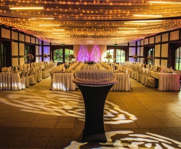 Elegant wedding banquet with draped fairy-light ceiling, long white tables, floral centerpieces and stacked champagne glasses.