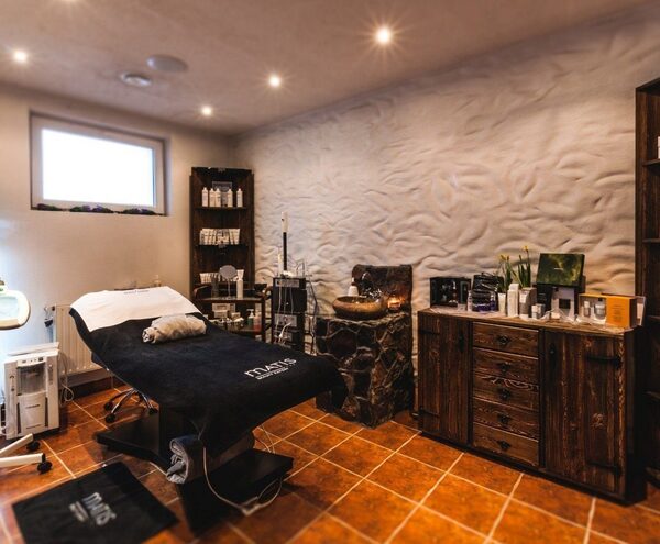 Cozy spa room with adjustable bed, professional skincare shelves, magnifying lamp, stone sink and warm lighting