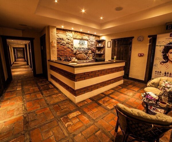 Warm, rustic hotel reception with brick-and-stone desk, terracotta tiled floor, cozy seating with flowers and hallway to rooms.