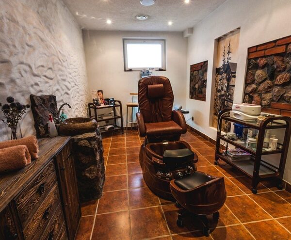 Private spa pedicure room with leather reclining chair and foot bath, stone sink, wooden cabinets and product trolley