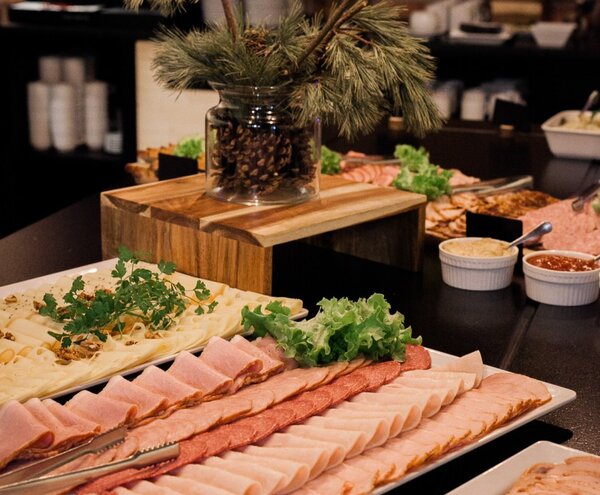 Buffet platter of neatly sliced cold cuts and cheeses with lettuce, condiments and a rustic pine-and-cone centerpiece