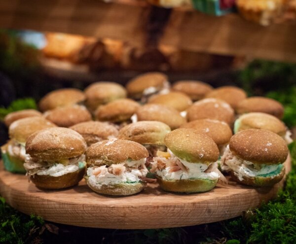 Assorted mini sliders on a wooden platter, soft brown buns filled with creamy cheese and flaked salmon, buffet display