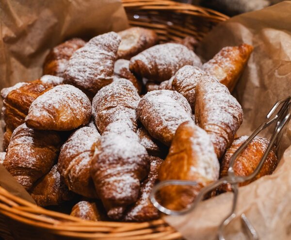 Basket of freshly baked powdered-sugar croissants on parchment with serving tongs, ideal for hotel breakfast