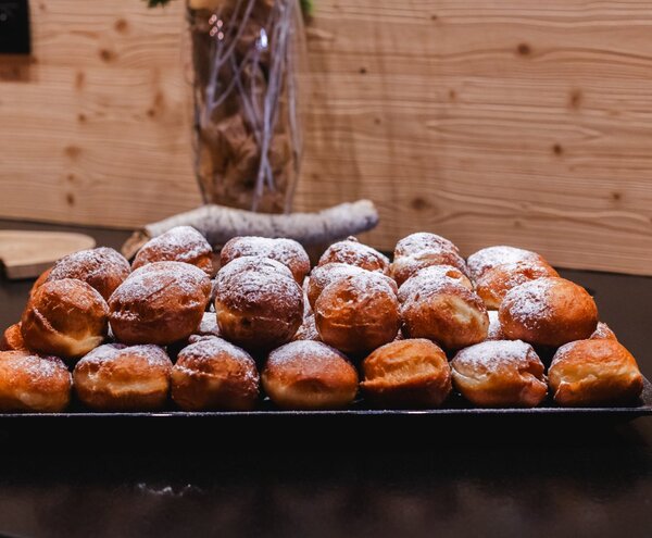 Złociste nadziewane pączki posypane cukrem pudrem na czarnym półmisku, podane na przytulnym drewnianym bufecie śniadaniowym