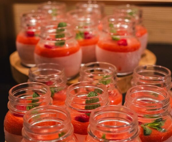 Individual strawberry mousse in glass jars with raspberry coulis and mint, arranged on wooden serving stands