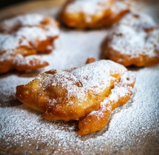 Golden fried pastries dusted with powdered sugar on a wooden board — warm breakfast or dessert treat.