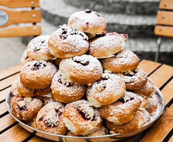 Powdered sugar–dusted, jam-filled pastries stacked on a serving platter on an outdoor café table