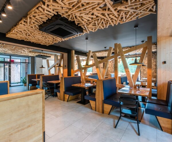 Nowoczesna restauracja hotelowa z drewnianymi boksami, granatowymi siedziskami, rzeźbionym sufitem i lampami wiszącymi.