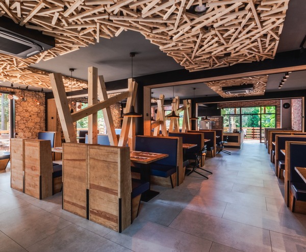 Restauracja hotelowa w stylu rustykalno‑nowoczesnym z drewnianymi boksami, dekoracyjnym sufitem z listew, lampami i oknami z widokiem na las