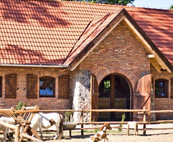 Brick country guesthouse with red tiled roof, wooden shutters and arched double doors, fenced paddock with ponies grazing