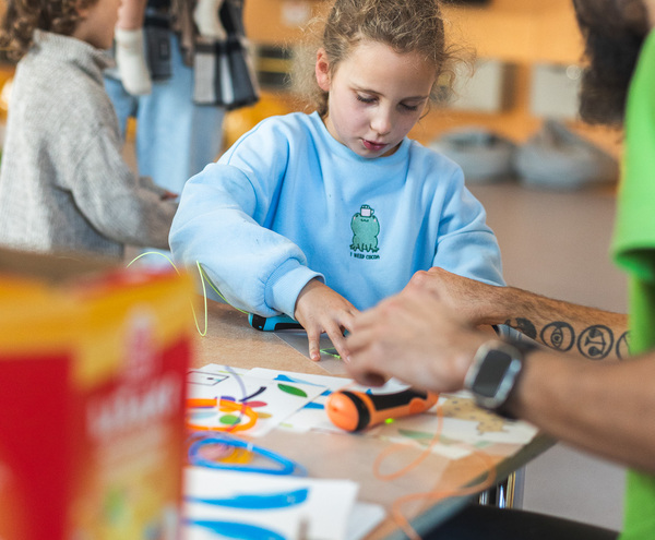 Hotel kids' craft table in a bright family play area — girl focused on a paper craft while an adult assists