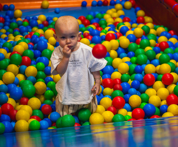 Toddler standing in a colorful indoor ball pit in a hotel's children's play area with padded walls and safety netting.