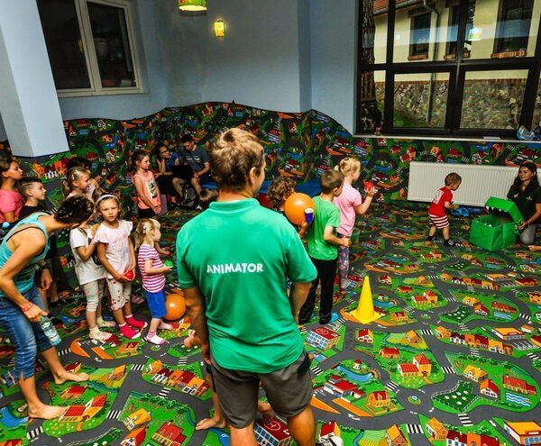 Vibrant hotel kids' club with an animator leading children playing with balls on a colorful town-map play carpet in a cozy activity room