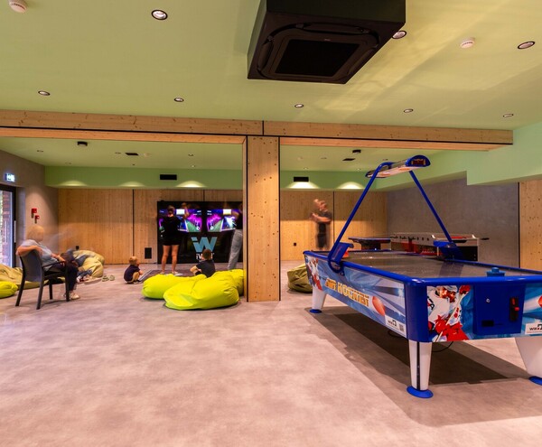 Pokój gier rodzinnych z stołem do air hockey, dużym ekranem do gier, limonkowymi pufami i drewnianymi panelami