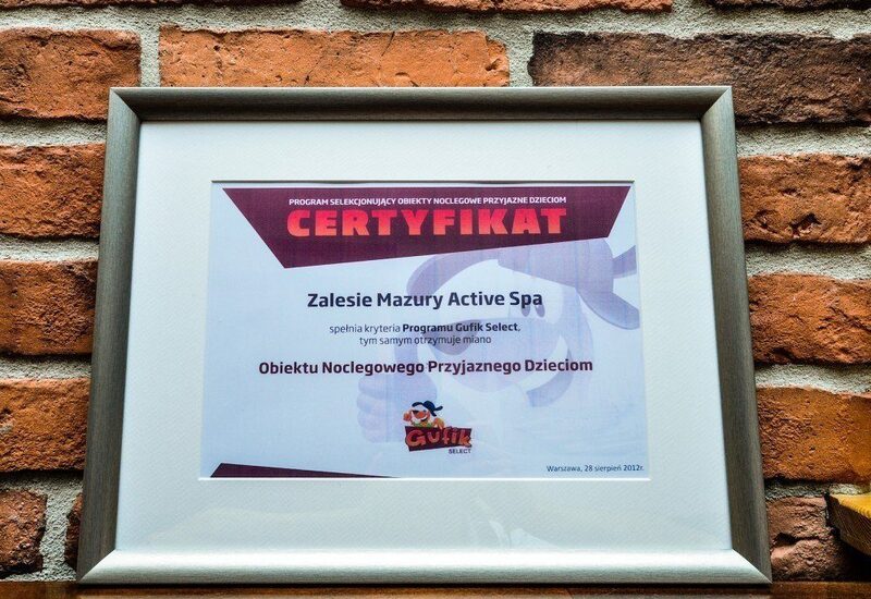 Oprawiony certyfikat na ceglanej ścianie potwierdzający, że Zalesie Mazury Active Spa to obiekt przyjazny dzieciom