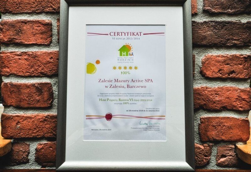 Oprawiony certyfikat na ceglanej ścianie potwierdzający 100% ocenę Zalesie Mazury Active SPA w Zalesiu, Barczewie jako hotel przyjazny rodzinie.