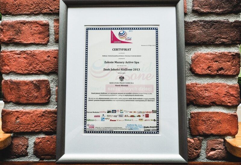 Certyfikat KidZone 2013 w srebrnej ramie na ceglanej ścianie — wyróżnienie rodzinnego spa Zalesie Mazury Active Spa.