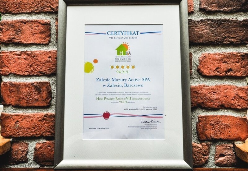 Oprawiony certyfikat hotelu Zalesie Mazury Active SPA wiszący na ceglanej ścianie nad drewnianą półką