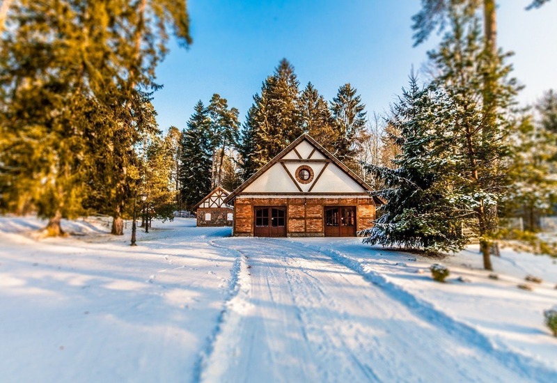 Drewniano-ceglana chata w stylu alpejskim z okrągłym oknem w szczycie, zaśnieżonym podjazdem ze śladami i sosnowym lasem w miękkim zimowym świetle