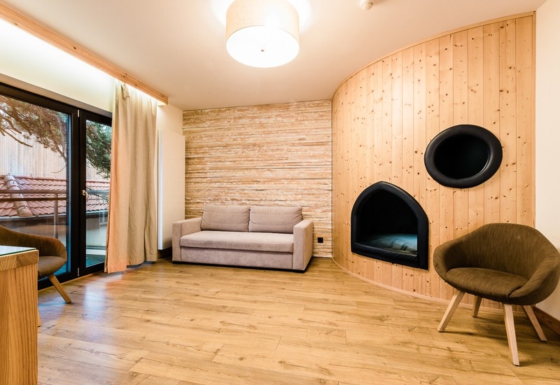 Przytulny salon z sofą, dwoma fotelami, zaokrągloną drewnianą ścianą z czarnymi wnękami do siedzenia oraz drzwiami na balkon