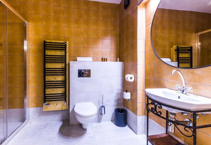 Łazienka hotelowa z terakotą, wiszącą toaletą, szklaną kabiną prysznicową, grzejnikiem na ręczniki, okrągłym lustrem i umywalką.