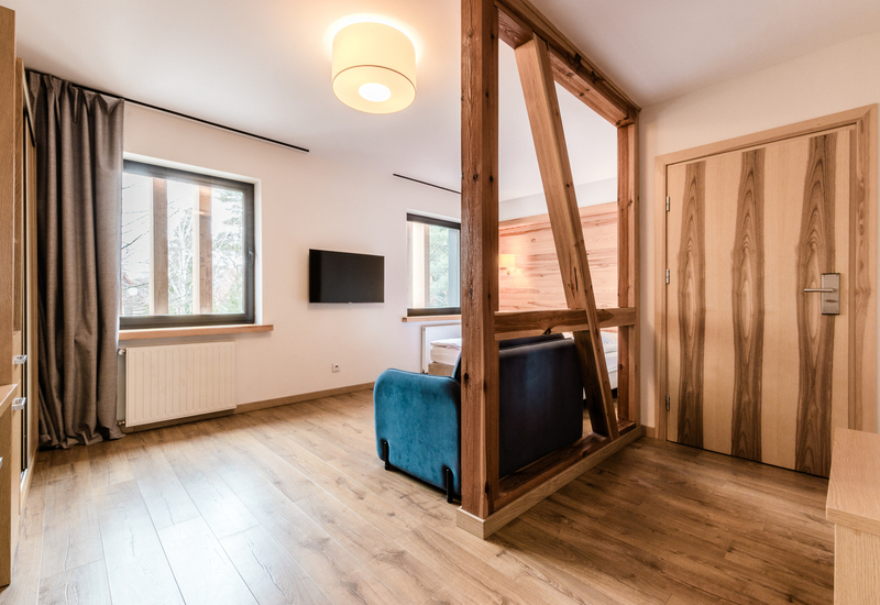 Przestronny, nowoczesny apartament z drewnianą przegrodą, turkusową sofą, telewizorem, drewnianą podłogą i przytulnym pokojem sypialnym.