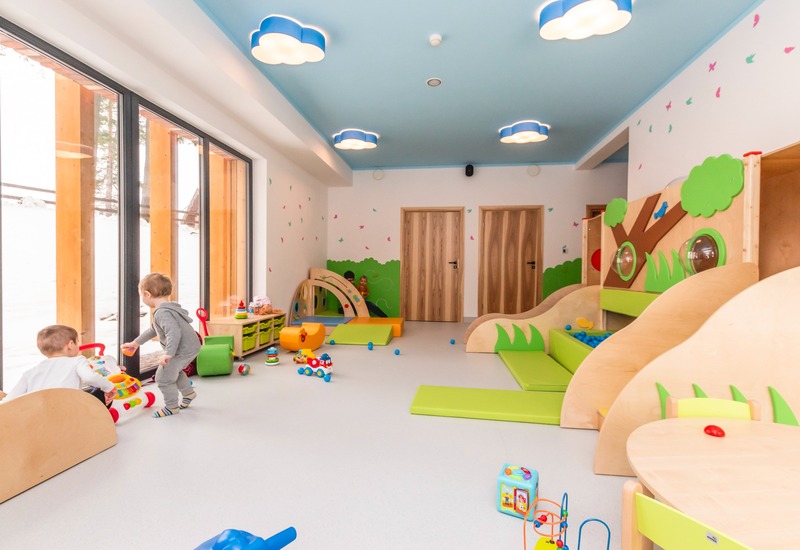 Jasne dziecięce centrum zabaw w hotelu z miękkimi modułami, basenem z piłkami, chmurkowymi lampami i dużymi oknami na śnieg