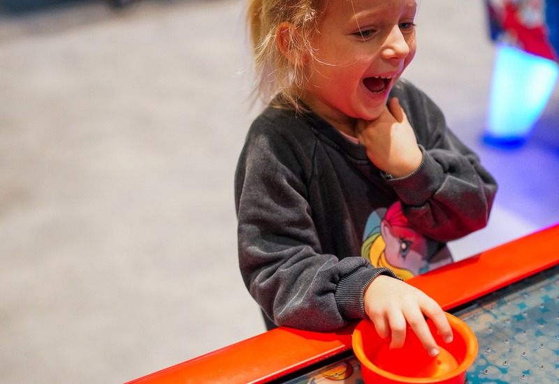 Dziewczynka śmieje się, grając przy kolorowym stole do air hockey w hotelowej sali gier rodzinnych