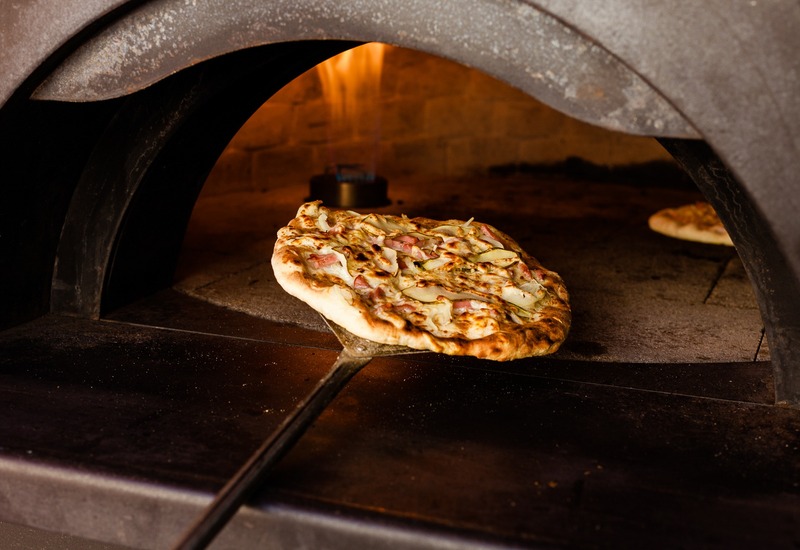 Pizza z pieca opalanego drewnem na łopacie, złocista skórka i roztopiony ser pod żarzącym się ogniem.