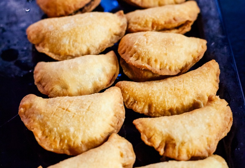 Złociste empanadas ułożone na czarnej tacy, ciepłe, pikantne przekąski idealne do bufetu lub serwisu pokojowego