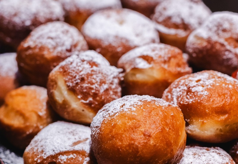 Ciepłe pączki posypane cukrem pudrem na bufetowej tacy — świeże wypieki śniadaniowe dla gości.