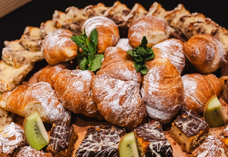 Talerz z wypiekami śniadaniowymi — rogaliki z cukrem, kawałki ciasta z czekoladą, plasterki kiwi i pomarańczy.
