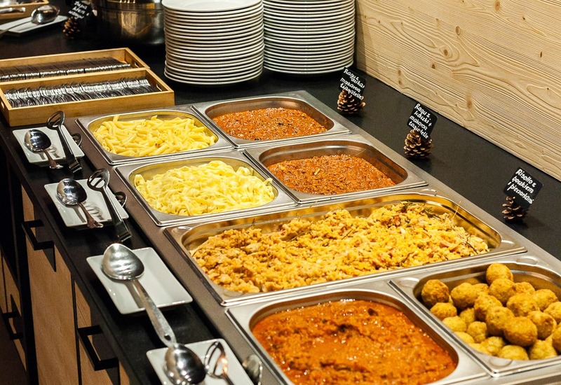 Bufet na ciepło z tacami makaronu, aromatycznym ragù, klopsikami, ustawionymi talerzami i sztućcami przy drewnie.