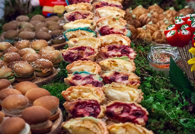 Bufet z rzędami owocowych i śmietankowych tart, mini burgerami, ptysiami i nadziewanymi pomidorkami