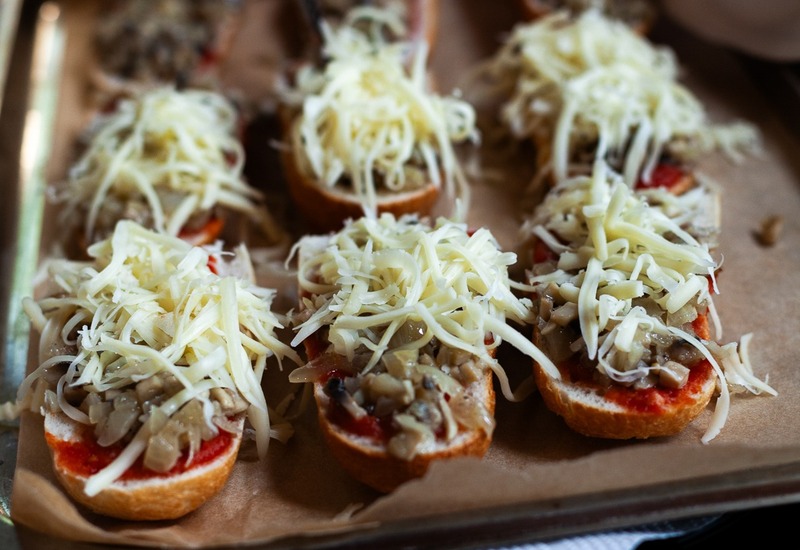 Taca crostini z sosem pomidorowym, podsmażonymi pieczarkami i startym serem, personel układa je szczypcami
