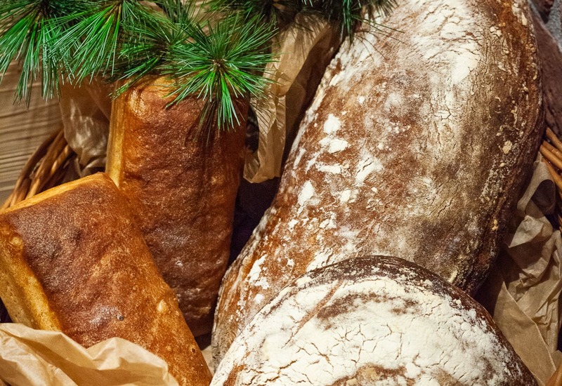 Kosz z rustykalnymi, mąką posypanymi bochenkami na papierze, ozdobiony sosnowymi gałązkami — pieczywo na śniadanie.