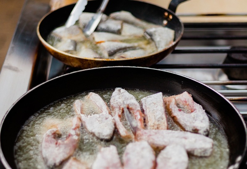 Szef kuchni w rękawiczce smaży obtoczone w mące filety rybne na patelniach — stacja live cooking dla hotelowego cateringu