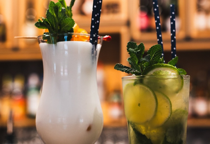 Kremowa piña colada z miętą i słomką w groszki obok limonkowego mojito ze świeżą miętą przy barze hotelowym.