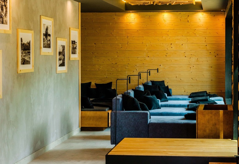 Przytulny salon hotelowy z niebieskimi sofami, czarnymi poduszkami, drewnianymi stopniami i dekoracyjnym drewnianym sufitem z ciepłym oświetleniem