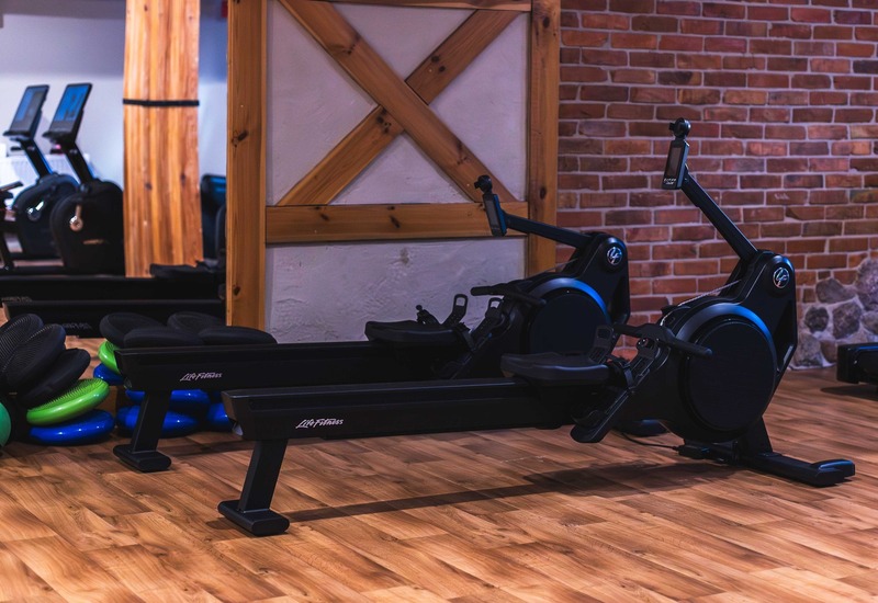 Hotelowa siłownia z maszynami wiosłowymi Life Fitness, poduszkami do równowagi, drewnianą podłogą i ceglaną ścianą