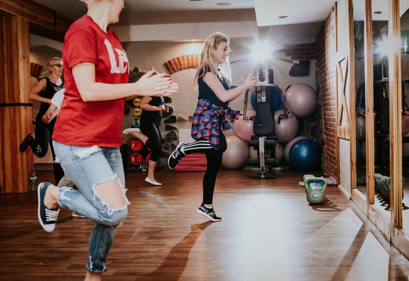 Sala fitness hotelu: zajęcia cardio prowadzone przez instruktorkę, drewniana podłoga, lustro, piłki i kettlebelle