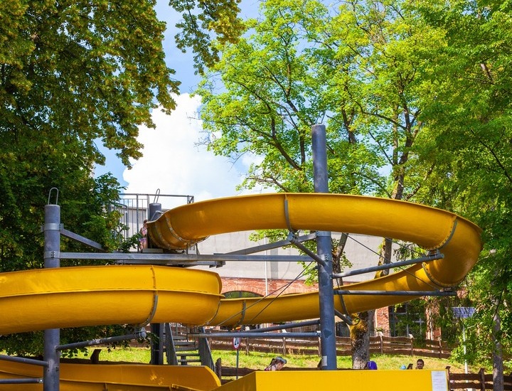 Żółta zjeżdżalnia wodna na zewnątrz, wijąca się wśród drzew nad kamienną podstawą przy hotelowym basenie rodzinnym.